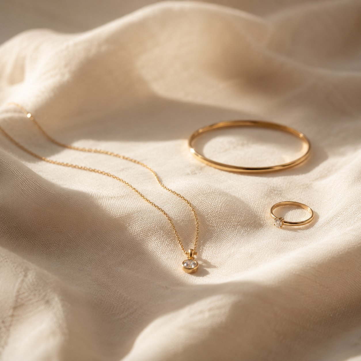 A fine gold-plated chain necklace, a polished bangle and a stone-set ring on ivory linen